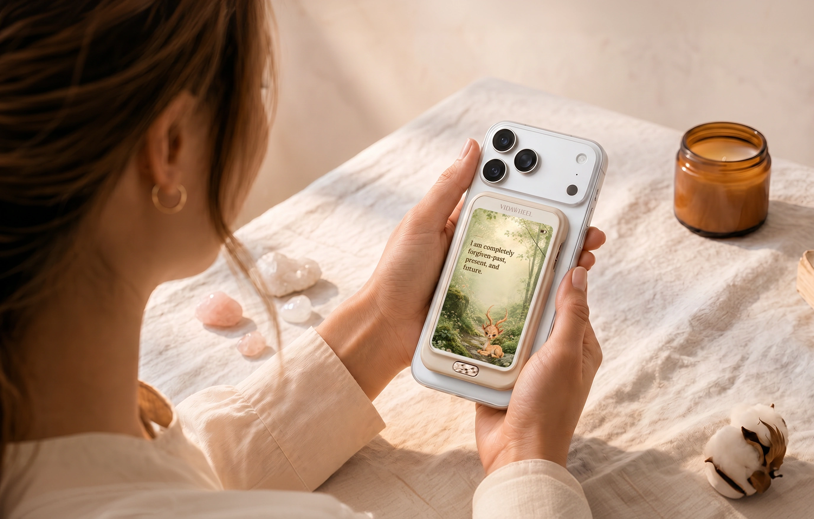 A hand holding an iPhone with a VidaWheel companion device outdoors in sunlit grass, showing a morning affirmation